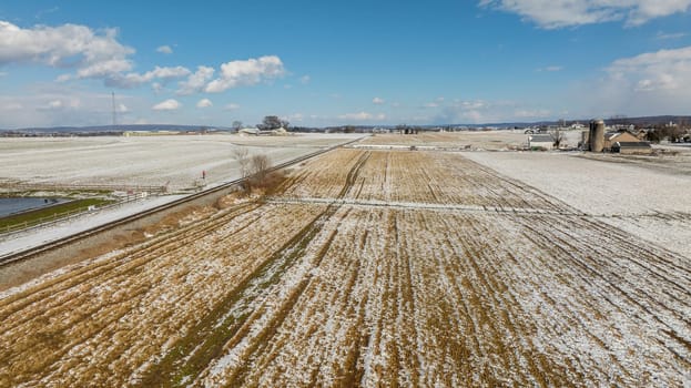 An Aerial View Of Snow-Dusted Farm Fields With A Railroad And Silos.