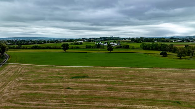 This aerial view showcases a striking rural landscape under an overcast sky, featuring contrasting patches of lush green fields and harvested areas.