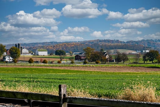 A rural landscape with a farmhouse and a barn. The sky is blue with some clouds