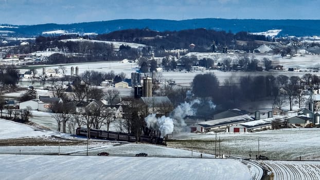 A train is traveling through a snowy countryside. The train is black and white and is the only thing visible in the image