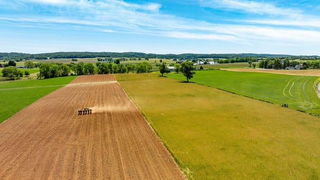 A field with a tractor in the foreground and a blue sky in the background. The field is mostly brown and green