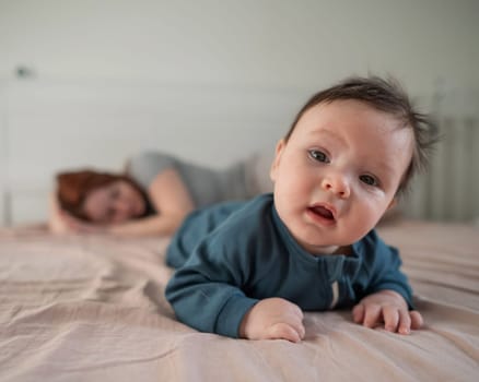 A three-month-old boy lies on his stomach on the bed and his mother sleeps behind him. Postpartum depression