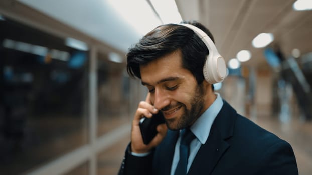 Smart business man calling phone while wearing headphone at train station. Professional executive manager talking to colleague about marketing strategy while waiting for train or subway. Exultant.