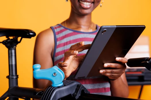 Detailed shot of healthy sports-loving black woman searching on phone tablet for bike maintenance. Close up shot of african american female holding smart device while maintaining bicycle.