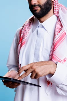 Man dressed in muslim white thobe and headscarf pressing on digital tablet touchscreen with fingers closeup. Arab wearing traditional clothes tapping on portable gadget screen