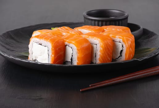 Philadelphia roll with salmon and cheese on plate on dark table.