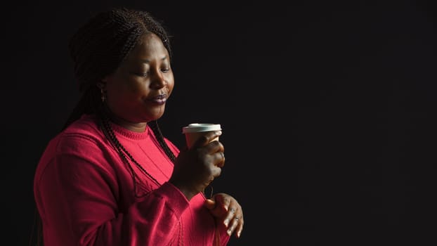 African american woman immersed in pleasure of sipping coffee lost in contemplation gazing upwards. Female fashion blogger savors her warm beverage with sense of satisfaction. Side-view portrait.