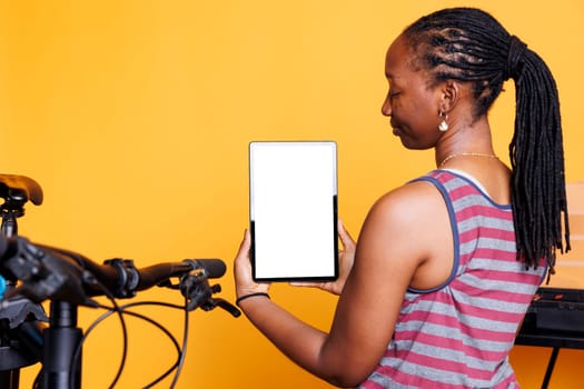 Close-up of a black woman holding digital tablet with an isolated whitescreen. African american lady carrying smart device with a blank chromakey template display for bicycle repair.