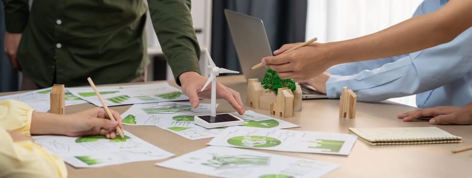 Windmill model represented renewable energy and wooden block represented eco city was placed on green business meeting table with environmental document scatter around. Front view. Delineation.