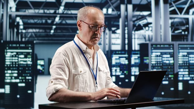 Certified technician expertly managing data while navigating in industrial server room. Professional ensuring optimal cybersecurity protection, optimizing systems and performing necessary updates