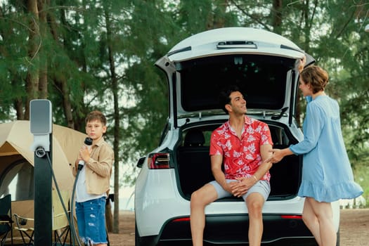 Outdoor adventure and family vacation camping in nature travel by eco friendly car for sustainable future. Lovely family recharge EV car with EV charging station in campsite. Perpetual