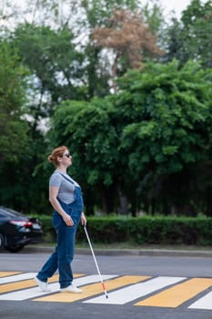 Blind pregnant woman crosses the road at a crosswalk with a cane