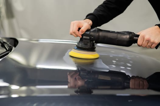 A mechanic polishes the surface of the hood of a gray car