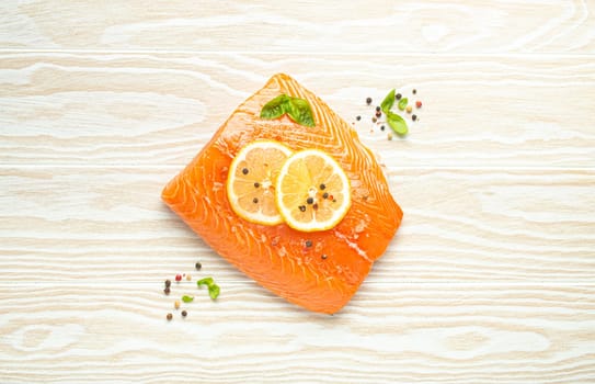 Fresh raw salmon marbled fillet on white rustic wooden table background with lemon, coarse salt, green herbs top view. Healthy cooking and balanced diet.