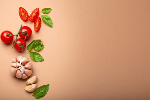 Food cooking border with cherry tomatoes, fresh green basil and garlic cloves top view on simple clean paper background, ingredients for preparing meal, copy space.