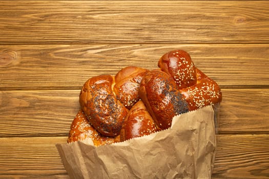 Freshly baked Challah bread covered with poppy and sesame seeds in a paper bag, top view on rustic wooden background, traditional festive Jewish cuisine.