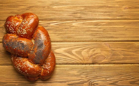 Freshly baked Challah bread covered with poppy and sesame seeds, top view on rustic wooden background, traditional festive Jewish cuisine. Space for text.