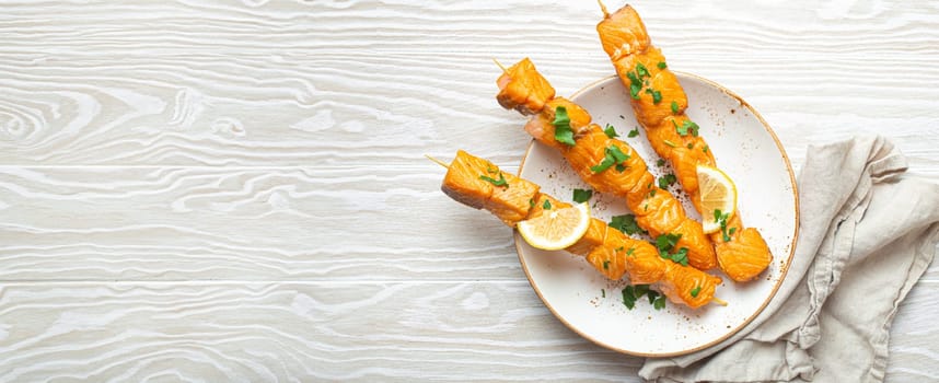 Grilled barbecue salmon skewers seasoned with green parsley and lemon on ceramic plate on white wooden rustic table background top view, healthy eating. Copy space