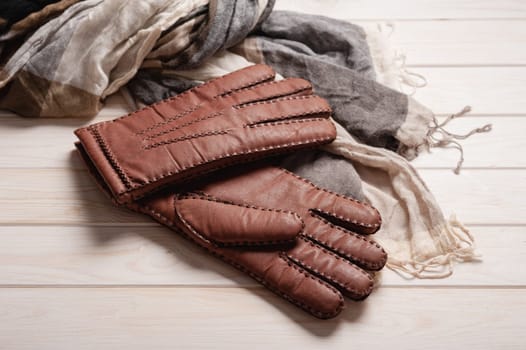 Pair of men's brown leather gloves and other men's accessories on wood background.