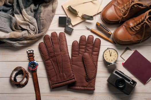 Pair of men's brown leather gloves and other men's accessories on wood background.