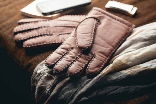 Pair of men's brown leather gloves and other men's accessories on wood background.