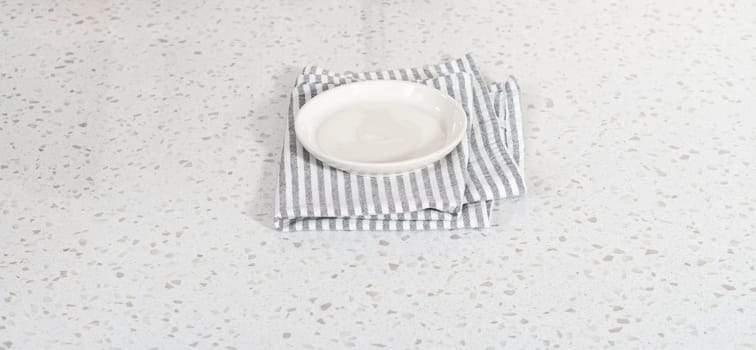 Empty a white plate with a kitchen towel on the white kitchen counter.