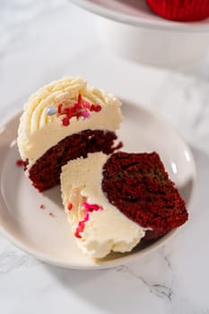 Sliced red velvet cupcakes with white chocolate ganache frosting on a white plate.