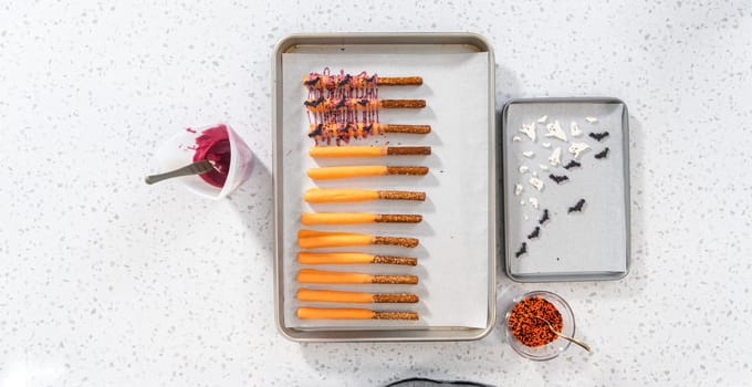 Flat lay. Dipping pretzel rods into melted chocolate to make Halloween chocolate-covered pretzel rods.