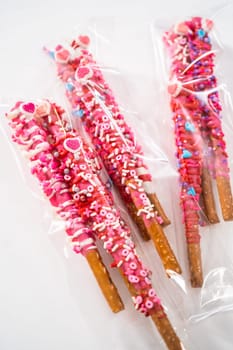 Chocolate-covered pretzel rods decorated with heart-shaped sprinkles for Valentine's Day packaged in a clear bags.