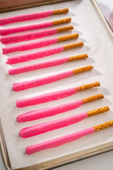 Dipping pretzels rods into silicone cup with melted chocolate to make chocolate-covered pretzel rods for Valentine's Day.