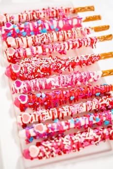 Chocolate-covered pretzel rods decorated with heart-shaped sprinkles for Valentine's Day.