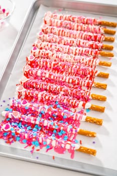 Drizzling melted chocolate over chocolate-dipped pretzels rods and decorating with sprinkles to make chocolate-covered pretzel rods for Valentine's Day.