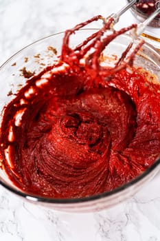 Mixing wet ingredients in a large glass mixing bowl to bake red velvet cupcakes with white chocolate ganache frosting.