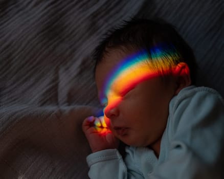 Close-up portrait of a newborn boy with a prism beam on his face. Rainbow