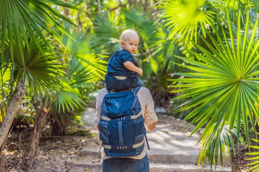 A man is joyfully carrying a baby on his shoulders through the lush jungle, surrounded by a variety of plants and wildlife. Both are smiling as they enjoy the natural landscape and leisurely stroll
