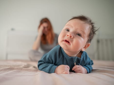 A three-month-old boy lies on his stomach on the bed and his mother sits behind him and cries. Postpartum depression