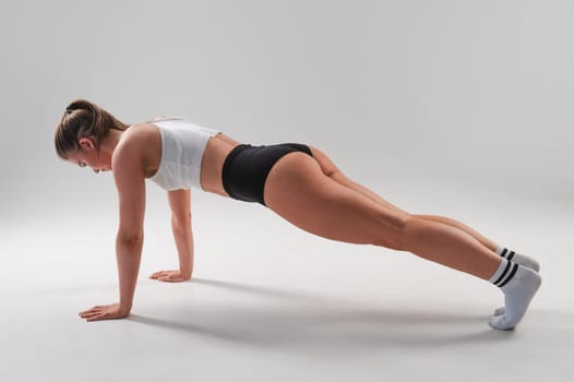 Athletic woman in shorts doing plank on white background