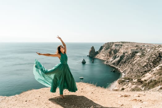 Woman green dress sea. Female dancer posing on a rocky outcrop high above the sea. Girl on the nature on blue sky background. Fashion photo