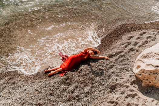 Woman red dress sea. Female dancer in a long red dress posing on a beach with rocks on sunny day.