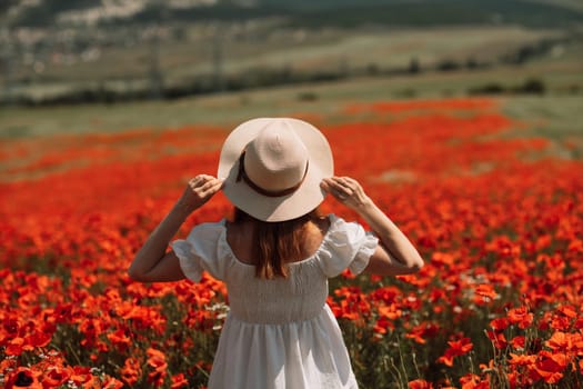 Field poppies woman. Happy woman in a white dress and hat stand through a blooming field of poppy raised her hands up. Field of blooming poppies