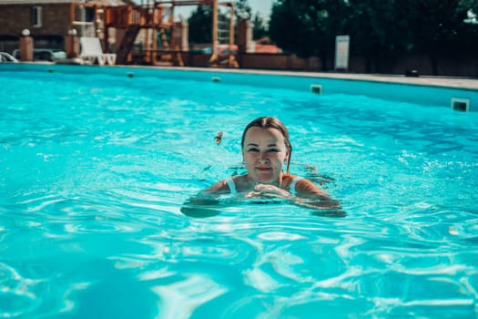 A woman is swimming in a pool. She is smiling and looking at the camera. The pool is blue and the water is calm