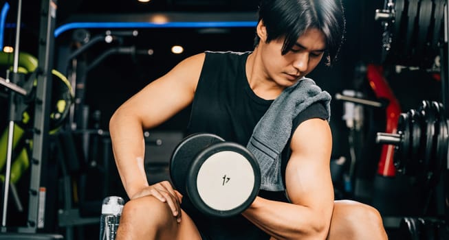 A fit and healthy young man sitting on a bench holding a dumbbell, working on his arm muscles and bicep, showcasing his dedication to maintaining a strong and muscular body. empty space