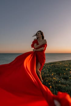 woman red dress standing grassy hillside. The sun is setting in the background, casting a warm glow over the scene. The woman is enjoying the beautiful view and the peaceful atmosphere