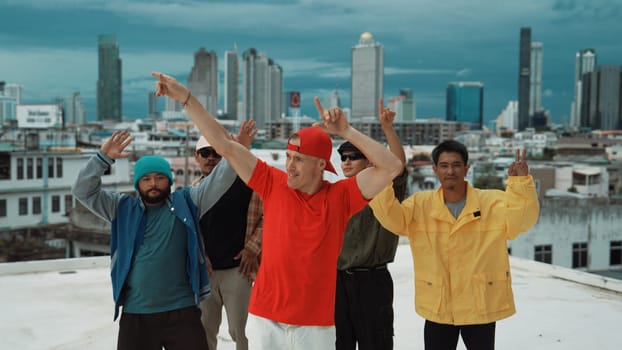 Multicultural teenagers dancing while looking at camera on rooftop with urban city view. Professional break dance group moving to hip-hop music with friends cheer. Outdoor sport 2024. Endeavor.