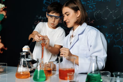 Teacher support schoolboy in laboratory. Schoolboy and teacher stand and experiment about science of chemistry in STEM class using liquid in glass container. Instructor mixing solution. Erudition.