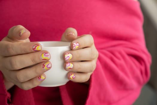 Pastel softness colorful manicured nails. Woman holding white cup of coffee or tea showing her new summer manicure in colors of pastel palette. Simplicity decor fresh spring vibes earth-colored neutral tones design