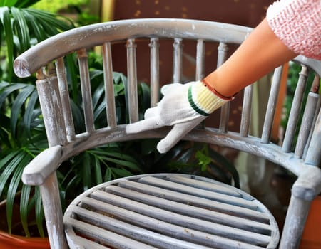 Garden chair with brush in protective gloves. Worker paints garden furniture. Renewal, renovation of wooden garden furniture