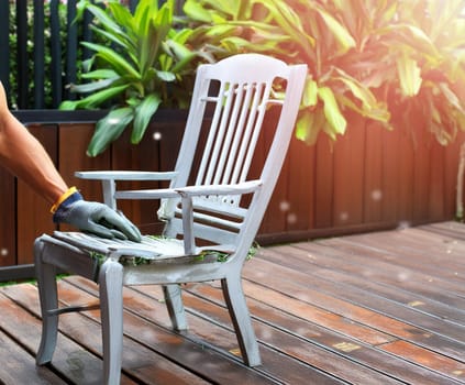 Garden chair with brush in protective gloves. Worker paints garden furniture. Renewal, renovation of wooden garden furniture