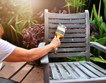 Garden chair with brush in protective gloves. Worker paints garden furniture. Renewal, renovation of wooden garden furniture