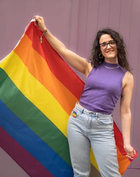 Front view portrait of happy lesbian young female holding a rainbow flag on her side. LGBT pride concept.